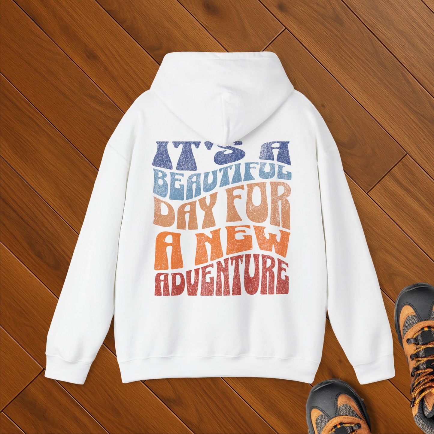 White hoodie with retro wavy lettering that reads “It’s a Beautiful Day for a New Adventure” in warm, earthy colors