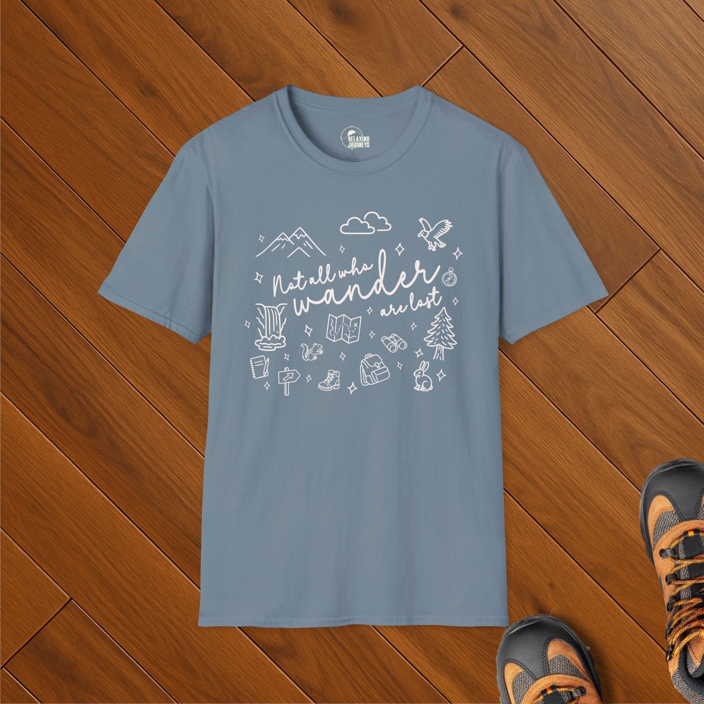 Blue t-shirt with white doodle illustrations of nature and hiking gear surrounding the phrase "Not all who wander are lost"