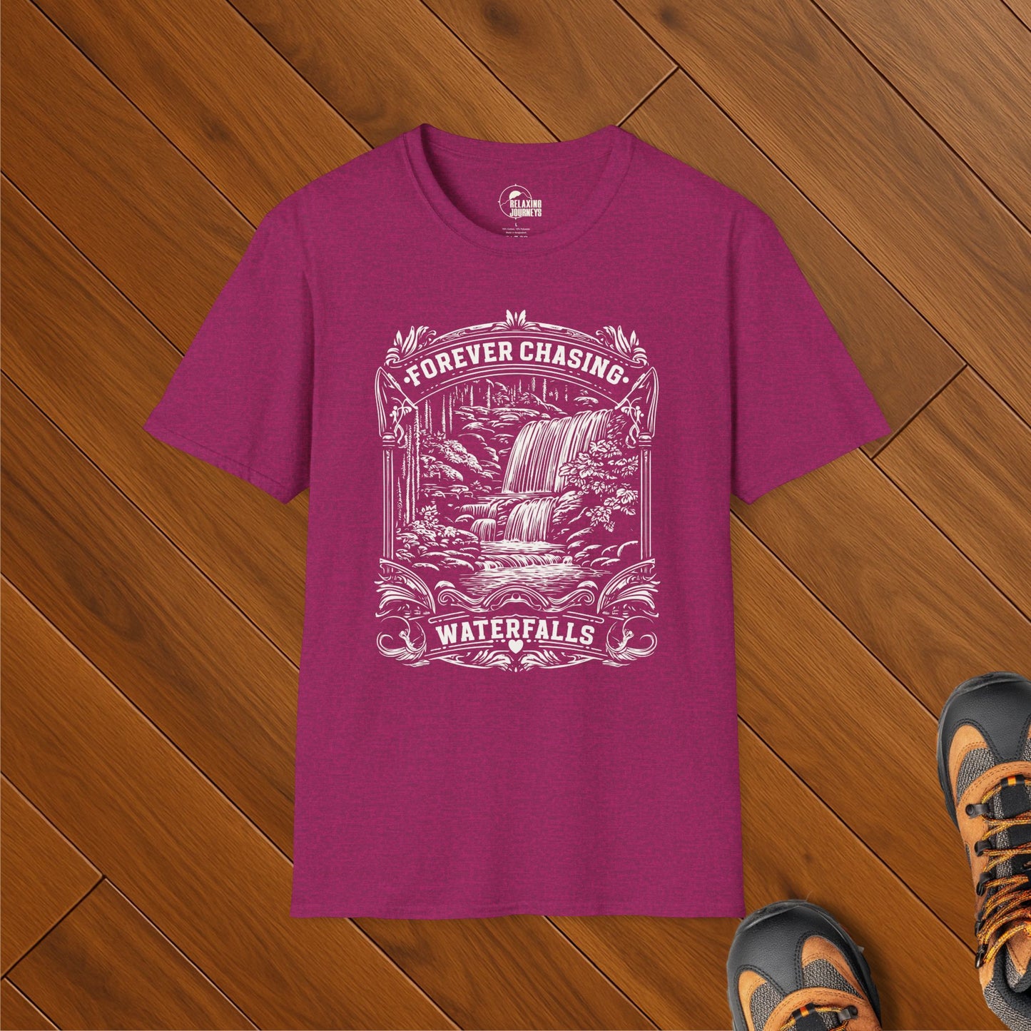 Heather maroon hiking t-shirt with vintage-style white print of a waterfall and the text “Forever Chasing Waterfalls.” Shirt is laid flat on wooden floor with hiking boots.