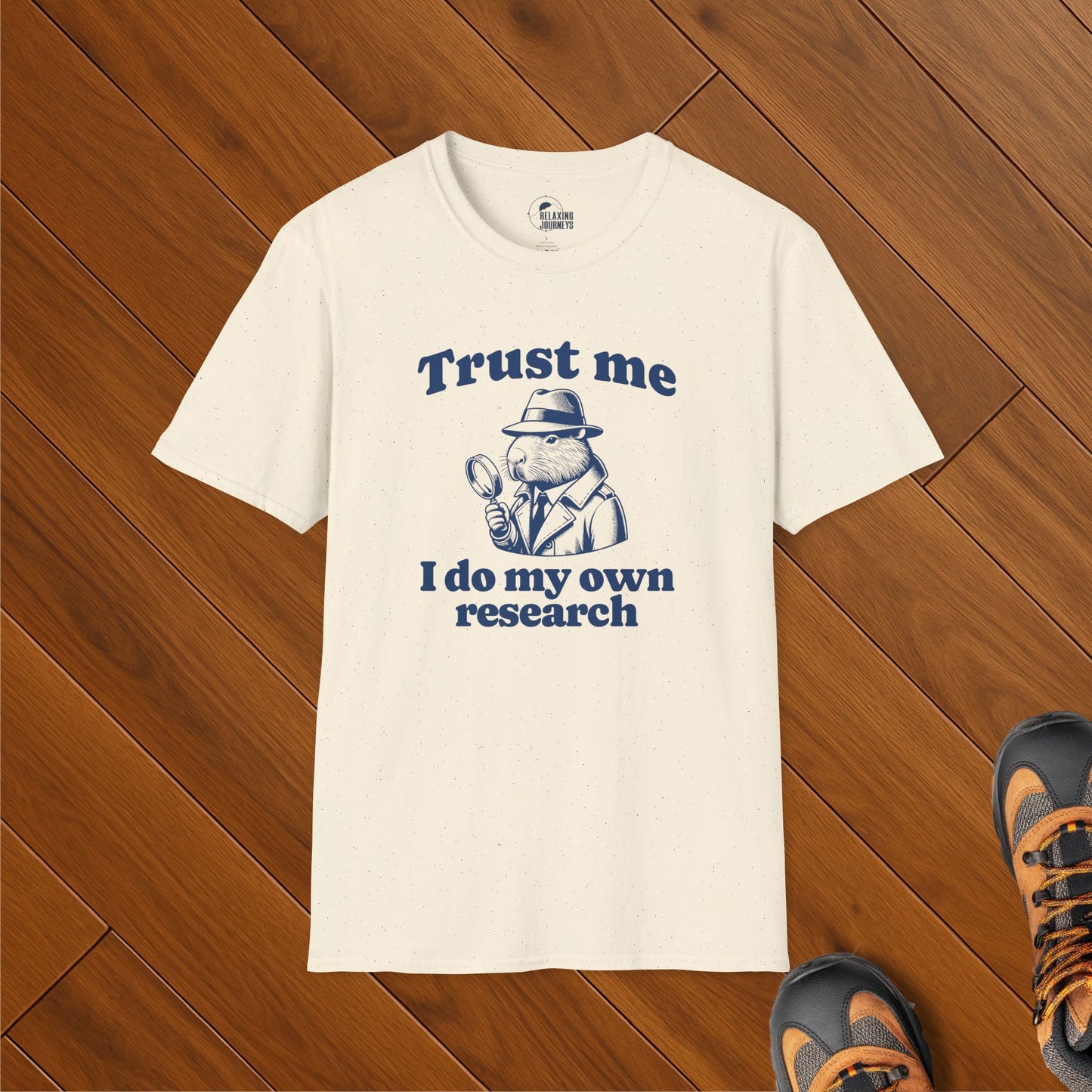 Cream t-shirt with vintage-style illustration of a capybara in trench coat holding magnifying glass, captioned "Trust me, I do my own research" – political satire meme shirt