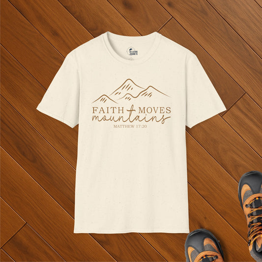 Cream speckled t-shirt with minimalist mountain graphic and text “Faith Moves Mountains – Matthew 17:20,” laid on wood floor with hiking boots
