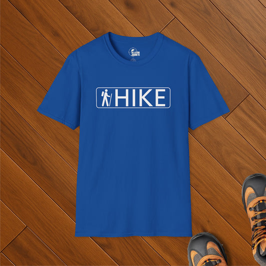 Royal blue t-shirt with white HIKE text and national park-style trail icon, laid on wood floor with hiking boots