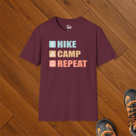 Maroon t-shirt with bold “Hike Camp Repeat” text and trail icon blocks, laid on wood floor with hiking boots