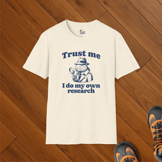 Cream t-shirt with vintage-style illustration of a capybara in trench coat holding magnifying glass, captioned "Trust me, I do my own research" – political satire meme shirt